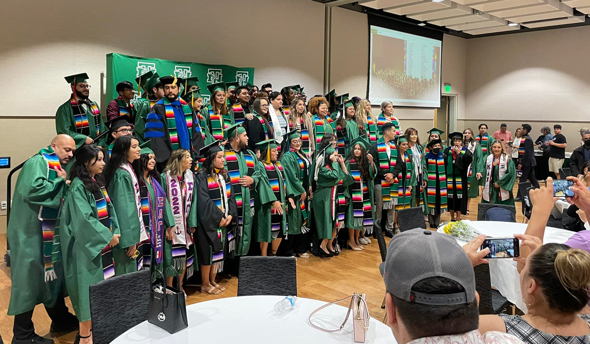 UNT students dressed in graduation robes pose for a photo.