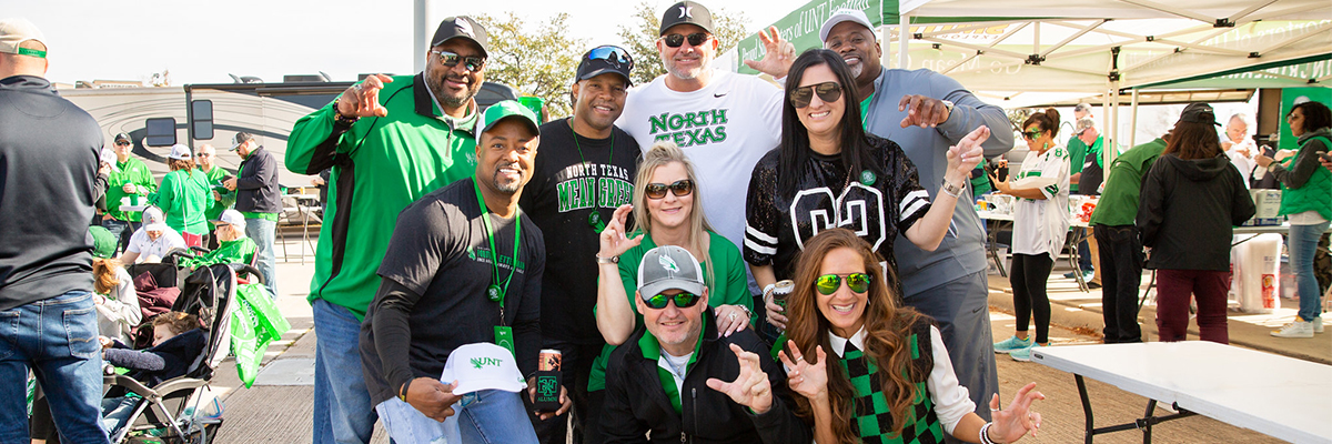 UNT alumni posing and smiling with eagle claws for a football game.