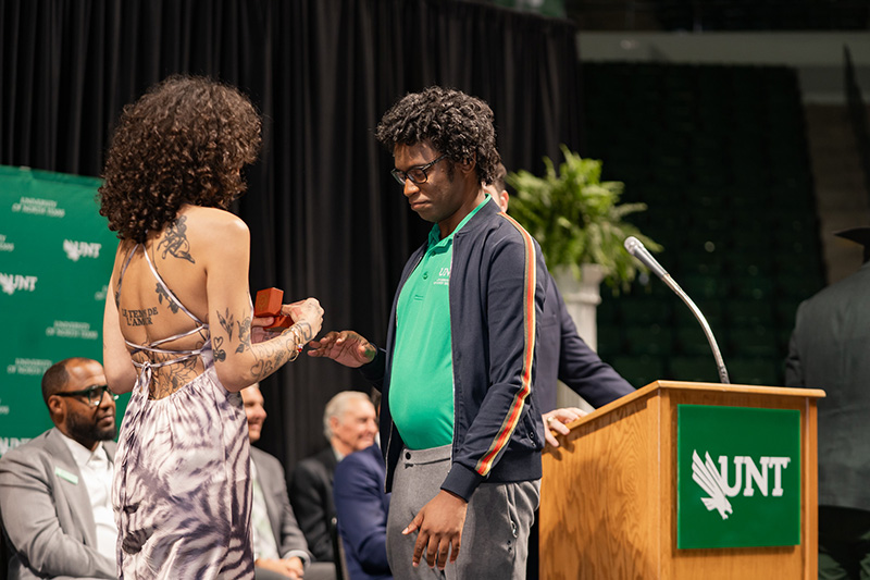 Corey Iles is presented his UNT class ring by a friend on-stage at the spring 2026 UNT Ring Ceremony.